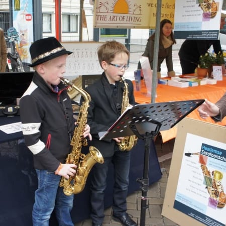 Twee jonge leerlingen spelen saxofoon bij een muziekstandaard