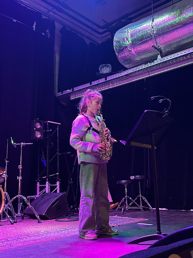 Leerling speelt saxofoon op het podium met paars licht
